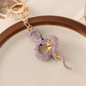 Goldener Schlangen Schlüsselanhänger mit lila Strass auf Keramikteller