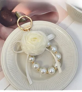 Detail of elegant satin rose and faux pearl keychain charm on a white ceramic plate