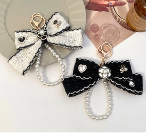Close-up of elegant camellia and pearl bow keychain charms on a stylish ceramic plate