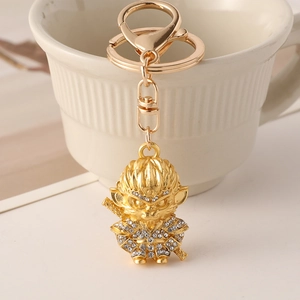 Gold Monkey King keychain with sparkling rhinestones leaning on a white ceramic cup