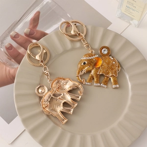 Porte-clés et broche éléphant doré avec strass et paillettes sur une assiette blanche