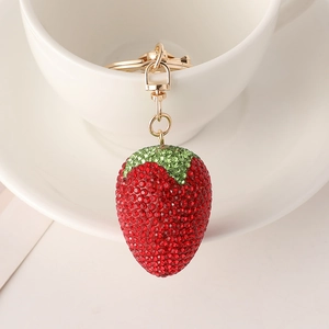Sparkling strawberry keychain with red rhinestones hanging on a white ceramic cup