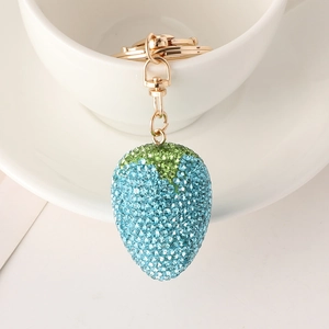 Close-up of a blue rhinestone strawberry keychain with gold hardware on a white ceramic cup