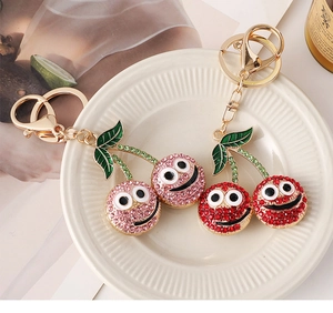 Close-up of sparkling rhinestone cherry keychains with smiley faces in a white tray