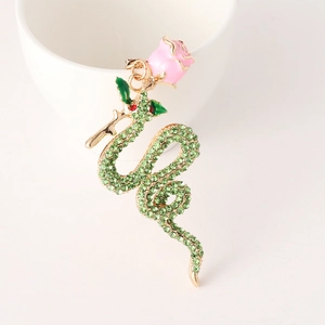 Golden snake keychain with pink enamel rose and green crystals on ceramic background