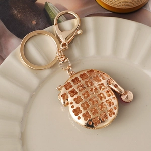 Golden keychain with hollow floral oval pendant displayed on a ceramic dish
