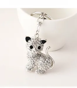 Dettaglio portachiavi a forma di gatto argentato con strass appoggiato a una tazza bianca