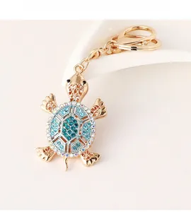 Detail of a golden turtle keychain with vibrant blue rhinestones on a white stand