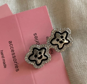 Close-up of star-shaped smiley face earrings with rhinestones on pink card