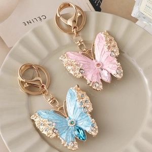 Elegant butterfly enamel keychain with rhinestones and pearls on a ceramic display