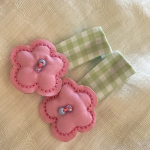 Close-up of pink fabric flower hair clips with pearl detail and green plaid ribbons