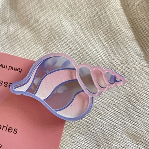 Dettaglio ravvicinato di un fermaglio per capelli a conchiglia sfumato rosa e viola su tessuto