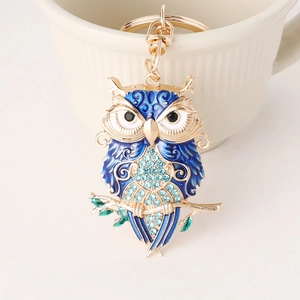 Blue owl keychain with rhinestones on a gold alloy branch next to a ceramic cup