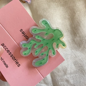 Dettaglio di un fermaglio per capelli in acrilico verde su carta rosa