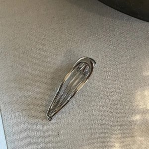 Detailed view of a metallic silver drop-shaped hair clip with a sleek mirror finish