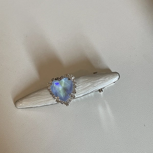 Détail d'une pince à cheveux blanc perle avec gemme cœur bleue et accents argentés brillants