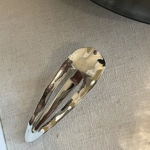 Macro detail of silver drop-shaped metal hair clip with liquid metal texture and polished finish