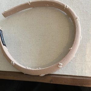 Detail shot of beige fabric headband with white embroidery and handmade tag logo
