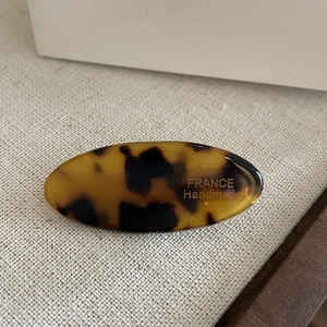 Oval tortoise shell hair clip with gold France Handmade logo on beige linen background