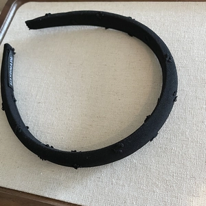 Detail of handmade black fabric headband with subtle dotted texture and brand label