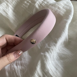 Detail of pink sponge headband with matte fabric and a gold 'Believe' engraved buckle