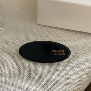 Detail of oval black acetate hair clip with gold France Handmade logo on linen