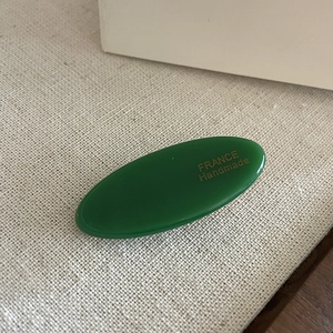 Detailed close-up of dark green oval hair clip with gold France Handmade logo engraving
