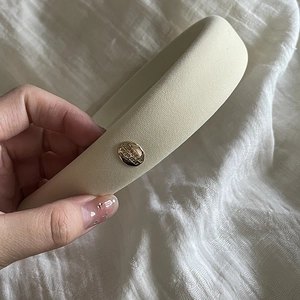 Close-up of cream thick sponge headband with gold metal buckle detail and text engraving