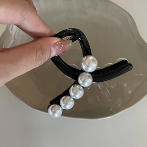 Dettaglio di un fermaglio per capelli nero lucido con cinque perle bianche decorative