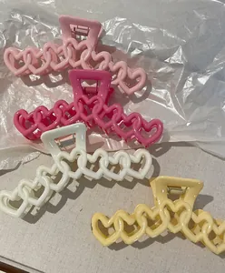 Dettaglio di grandi mollette per capelli a cuore vuoto in rosa, giallo e bianco su tessuto