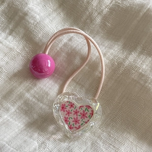 Détail d'élastique rose avec pendentif coeur transparent et petit motif floral