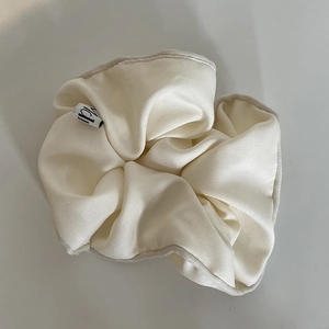 Macro detail of creamy white scrunchie showing fine fabric texture and brand label