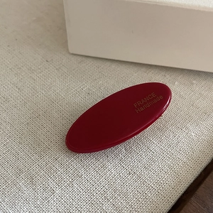 Detailed macro view of an oval burgundy acetate hair clip with golden handmade lettering