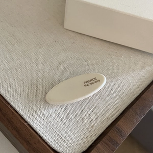 Detail view of cream white oval hair clip with France Handmade lettering on linen cloth