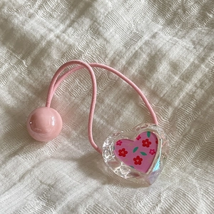 Détail d'un chouchou rose élastique avec un pendentif en cœur de cristal et motif fleuri