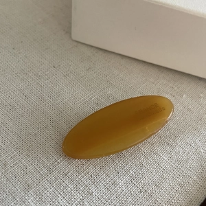 Detailed close-up of amber oval acetate hair clip with FRANCE handmade engraving on fabric
