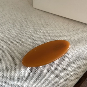 Detailed view of an oval amber acetate hair clip with smooth finish on textured fabric