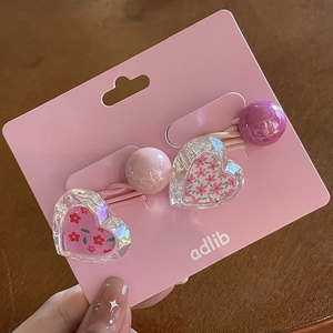 Détail de deux élastiques à cheveux roses avec breloques en forme de cœur sur carte rose