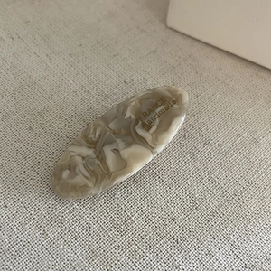 Close-up of an oval acetate hair clip with marble texture and golden handmade lettering
