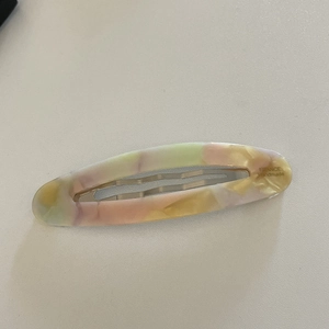 Detailed macro view of an oval acetate hair clip with marble texture and metal spring clip