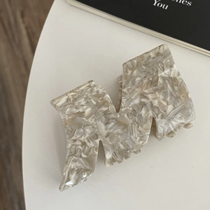 Macro view of M-shaped acetate shark hair clip with cream marble texture on white surface