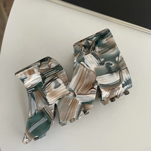 Macro view of a large acetate shark clip featuring premium marble texture in teal and beige