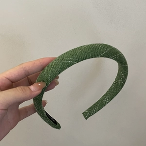 Dettaglio del cerchietto in maglia verde con trama a rombi ed etichetta Hand Made