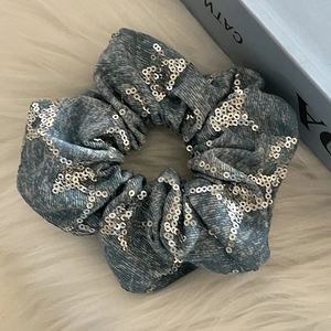 Détail d'un chouchou en denim bleu avec des paillettes argentées et une texture ondulée