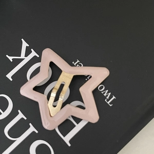 Pince à cheveux étoile rose avec ressort en métal doré sur fond noir décoratif