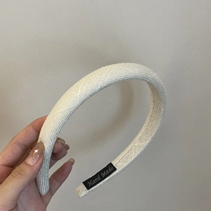 Dettaglio di un cerchietto intrecciato beige con etichetta Hand Made e trama del tessuto