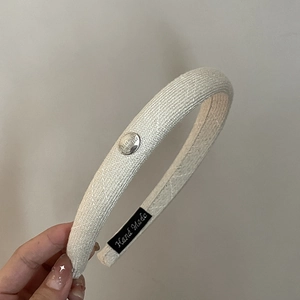 Détail d'un serre-tête en tissu crème avec breloque en métal argenté et étiquette faite main
