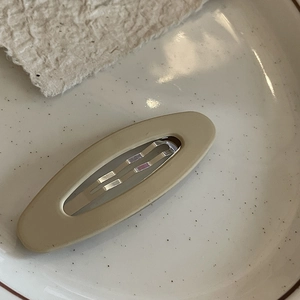 Matte finish khaki oval hair clip for women displayed on a ceramic dish