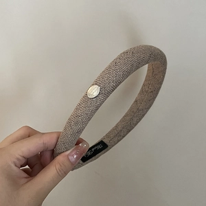 Détail d'un serre-tête en lin marron clair avec badge en métal argenté et étiquette tissée