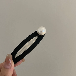 Detail view of a matte black oval BB hair clip with a large white pearl accent